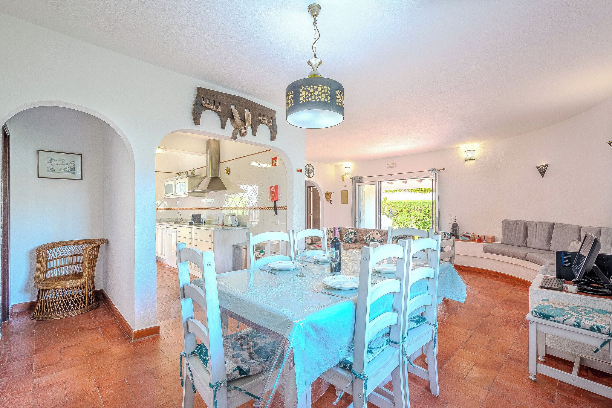 A dining area with a table set for six, white chairs, a chandelier, and a view of the kitchen and living area.