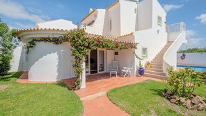 Eine weiße Villa mit einer überdachten Terrasse, Sitzgelegenheiten im Freien und einem Pool.
