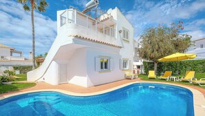 Eine moderne Villa mit Swimmingpool, Sonnenterrasse und einem Baum mit roten Blüten.