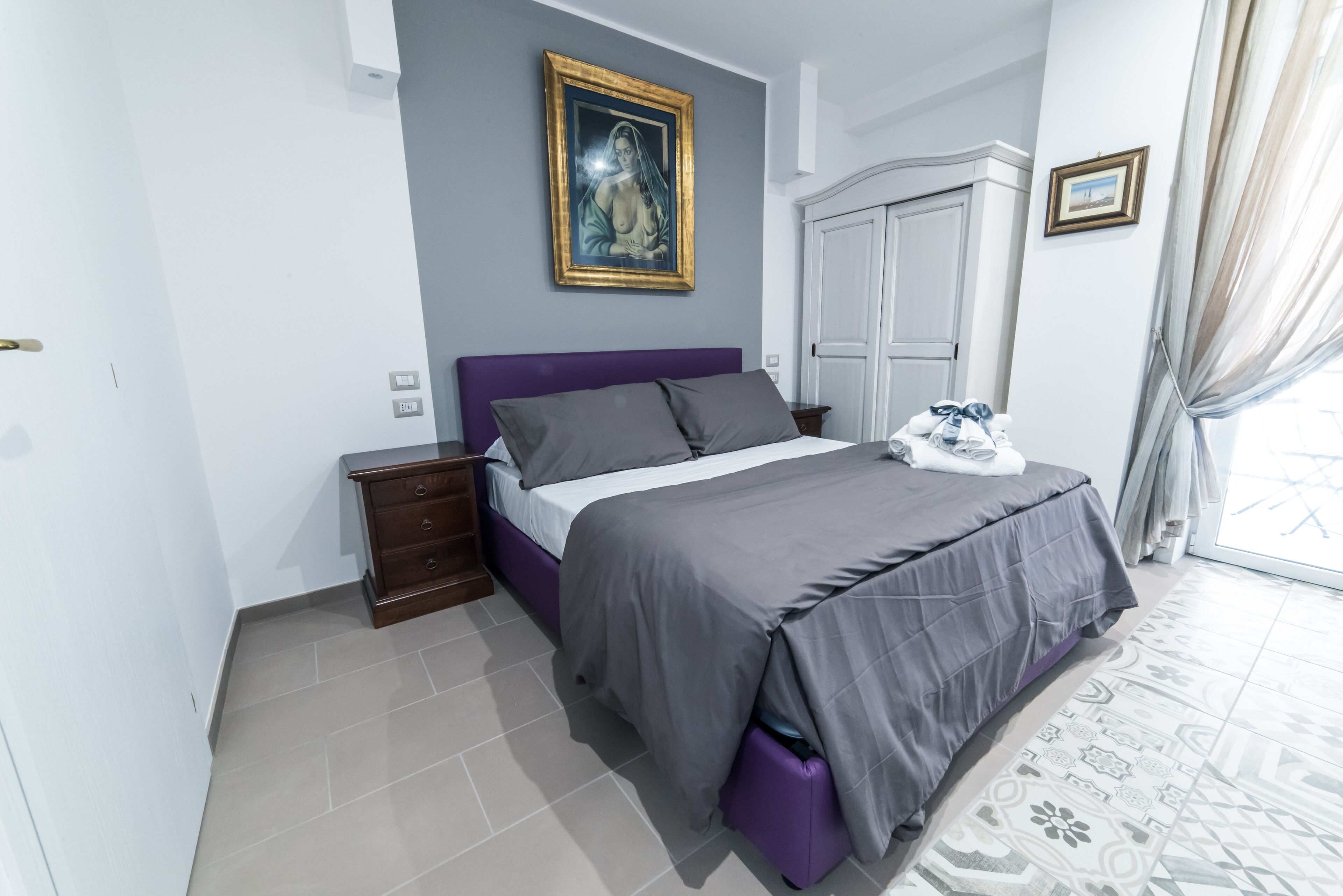 A bedroom with a bed, a dresser, a wardrobe, and a painting on the wall.