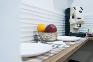 Una encimera de cocina con un bol de fruta, una cafetera y un mantel a cuadros.