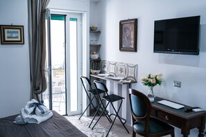 A hotel room with a bed, a desk with a chair, a TV, and a balcony with a view. - Le Berceau Di Salvatore De Tommaso (Naples)