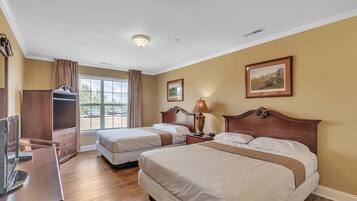 A hotel room with two beds, a desk, a TV, and a window with curtains.