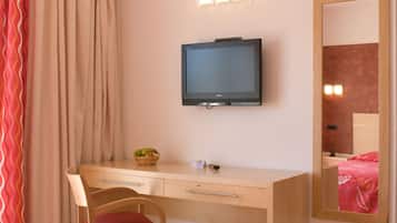 Un dormitorio con un escritorio de madera, televisión montada en la pared, un espejo y una cama con colcha roja.