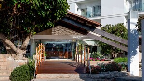 A hotel entrance with a wooden deck, stone steps, and a glass facade. - Hotel Capricho (Capdepera)