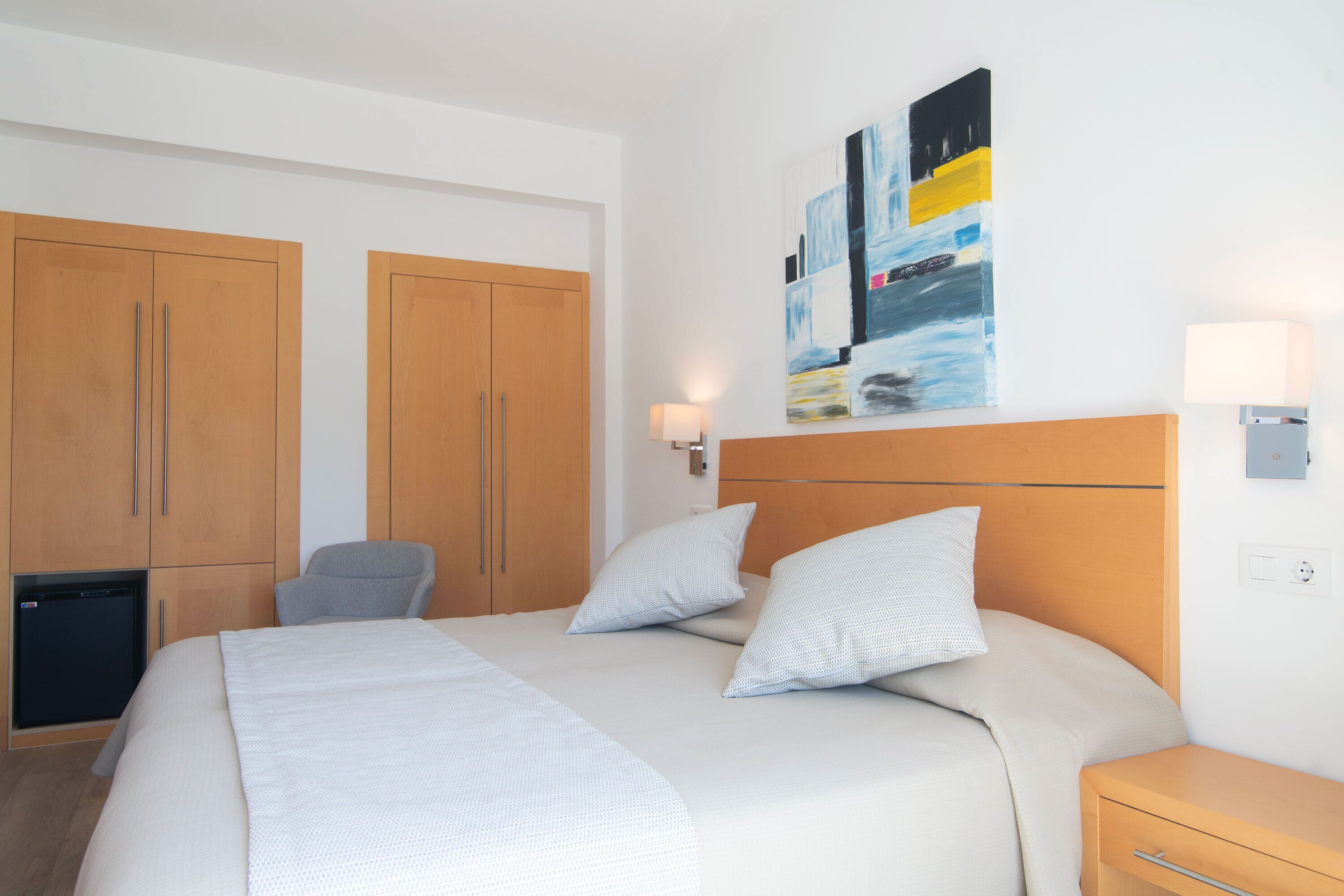 Een hotelkamer met een bed, twee houten kasten, een bureau, een stoel, een wanddecoratie en een lamp.