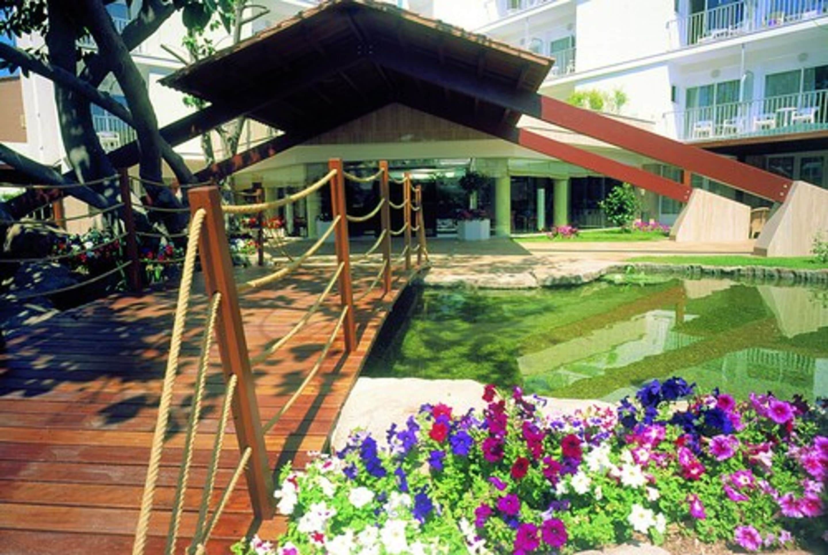 Eine Holzterrasse mit Seilzäunen, einem Pool und bunten Blumen.