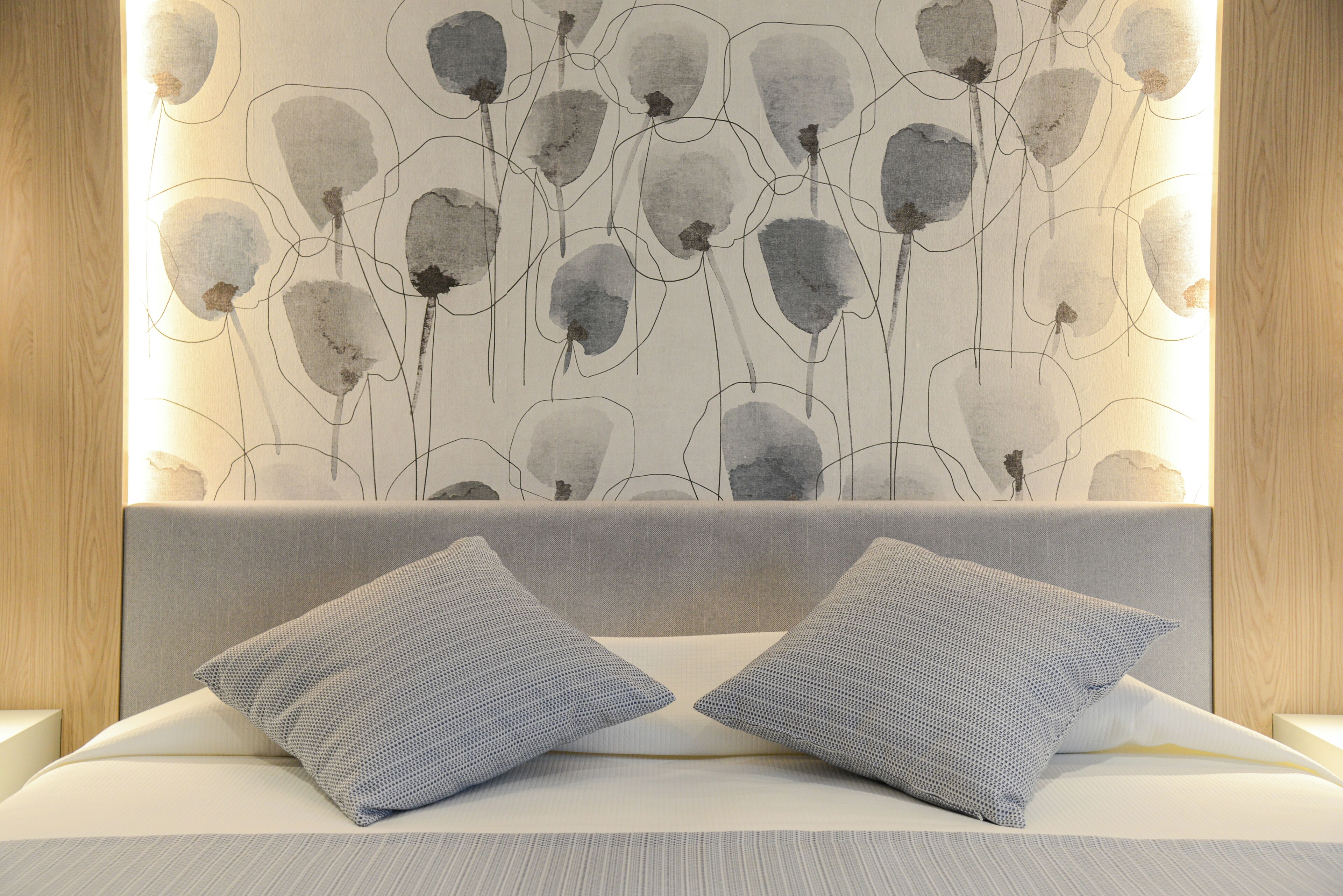 A bedroom with a grey headboard, two pillows, and a wall with abstract art.