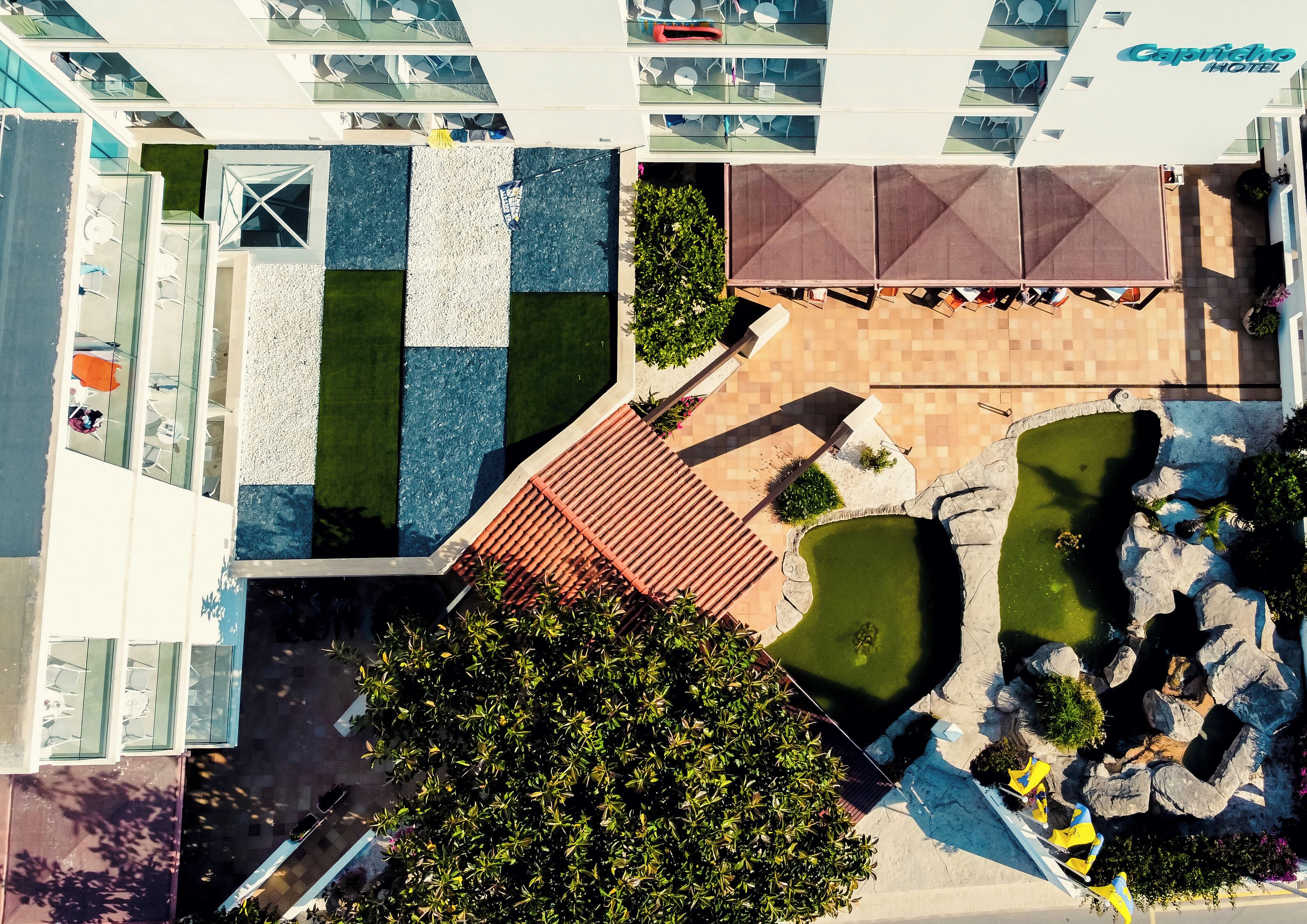 Vista aérea de un patio de hotel con piscina, mobiliario exterior y jardín de rocas.