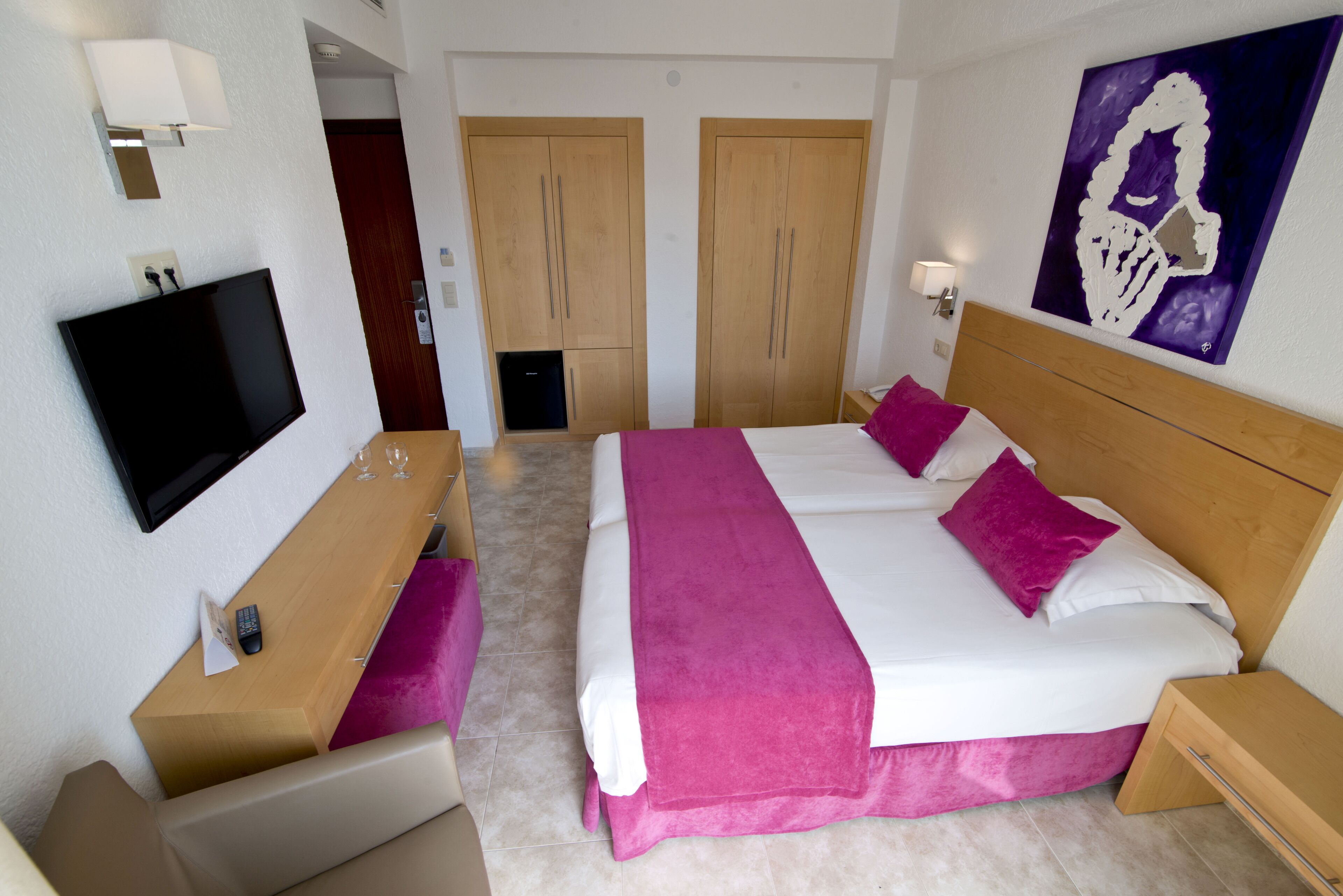 A hotel room with a bed, a TV, a desk, and a wardrobe.