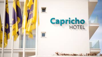 Un moderno cartel de hotel con el nombre "Capricho Hotel" y banderas en primer plano.