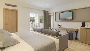 A modern hotel room with a large bed, a sofa, a desk, and a TV. - Hotel Capricho (Capdepera)