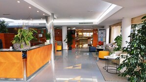 A modern hotel lobby with a reception desk, seating area, and a staircase leading to the upper floors. - Hotel Capricho (Capdepera)