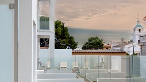 A modern building with a glass balcony, white walls, and a view of a church with a blue dome. - Hotel Capricho (Capdepera)
