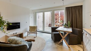 A modern living room with a flat-screen TV, comfortable seating, a dining area, and a sliding glass door leading to an outdoor patio. - Luxury beach studio incl. parking spot (Zandvoort)
