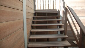 A wooden staircase with a metal handrail, leading to an outdoor area. - Luxury beach studio incl. parking spot (Zandvoort)