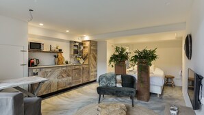 A modern living room with a dark grey sofa, a round wooden coffee table, and a kitchen area with a microwave and wooden cabinets. - Luxury beach studio incl. parking spot (Zandvoort)