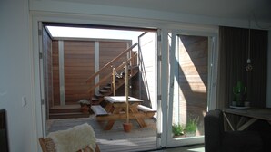 A room with a sliding glass door leading to an outdoor patio with wooden furniture and a staircase. - Luxury beach studio incl. parking spot (Zandvoort)