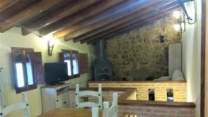 Ein rustikaler Essbereich mit einem Holztisch, weißen Stühlen, einem Fernseher und einer Steinsäule im Hintergrund.