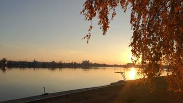 A calm lake at sunset with a dock and a tree in the foreground.
