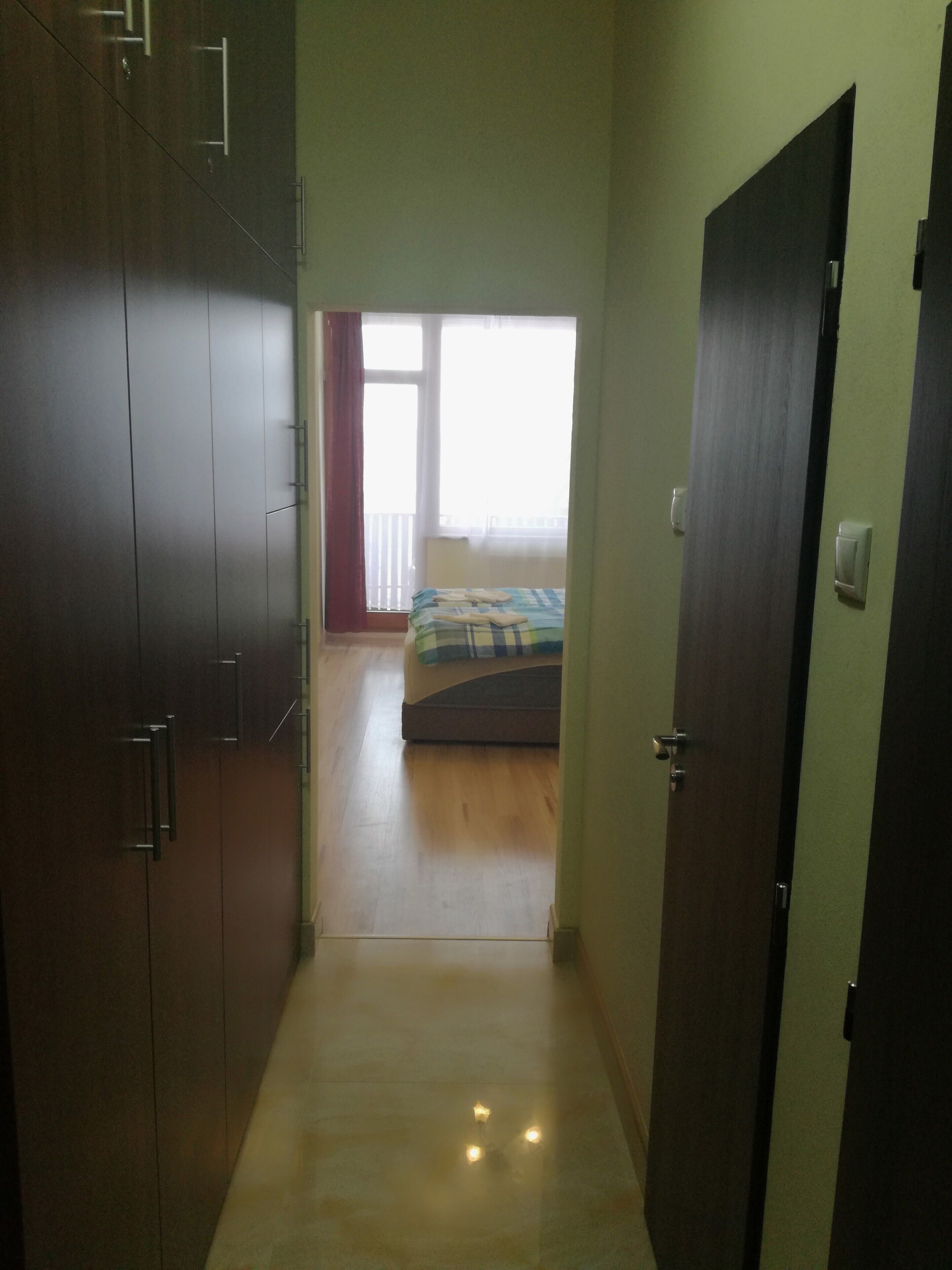 A narrow hallway leading to a bedroom with a bed and a window.