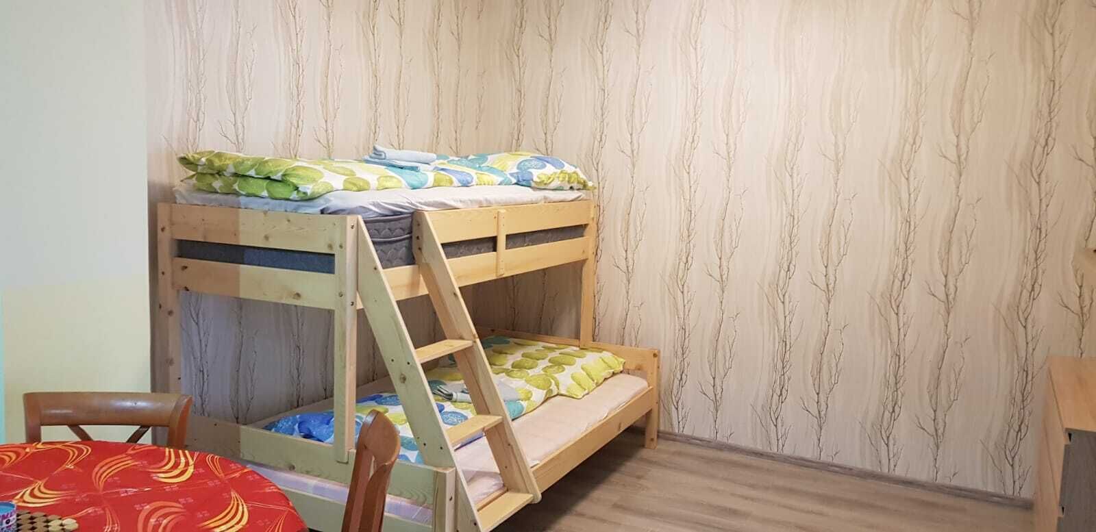 A bunk bed with a ladder, a wooden chair, and a table with a patterned tablecloth.