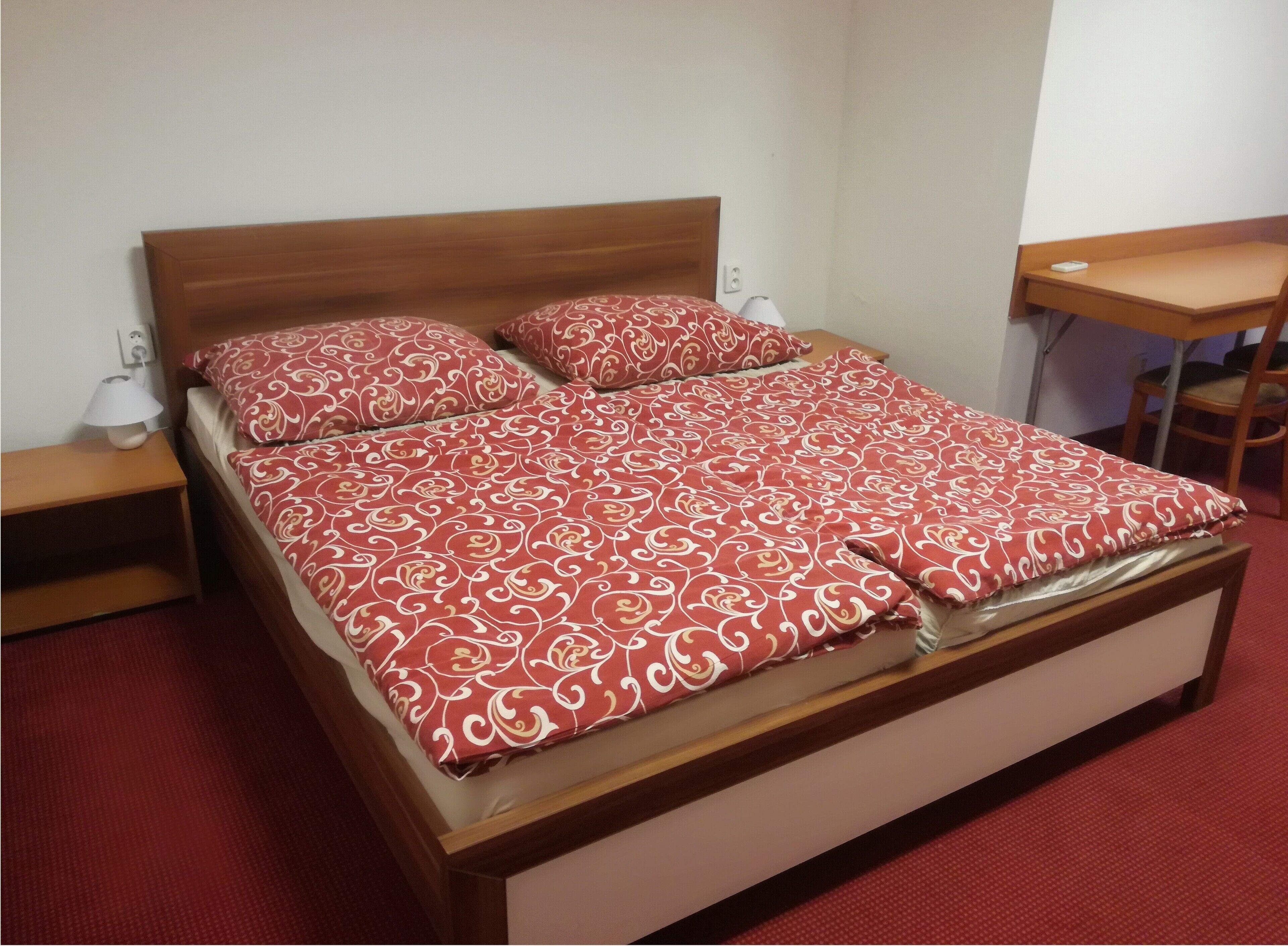 Una habitación de hotel estándar con una cama individual, una mesita de noche con lámpara y una pequeña mesa con una silla.