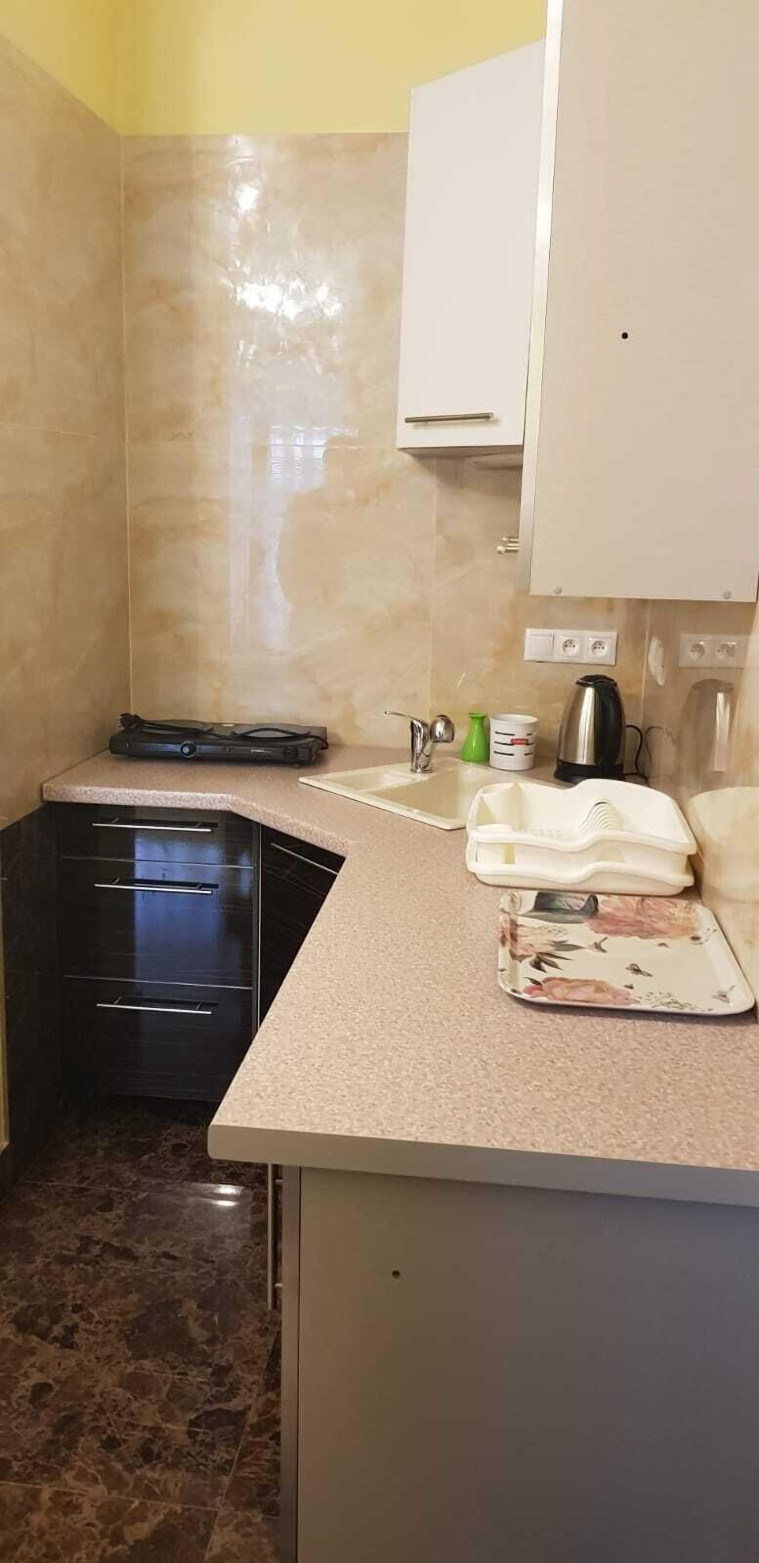A compact kitchen with a dark cabinet, a countertop with a kettle, a coffee maker, and a small plate.