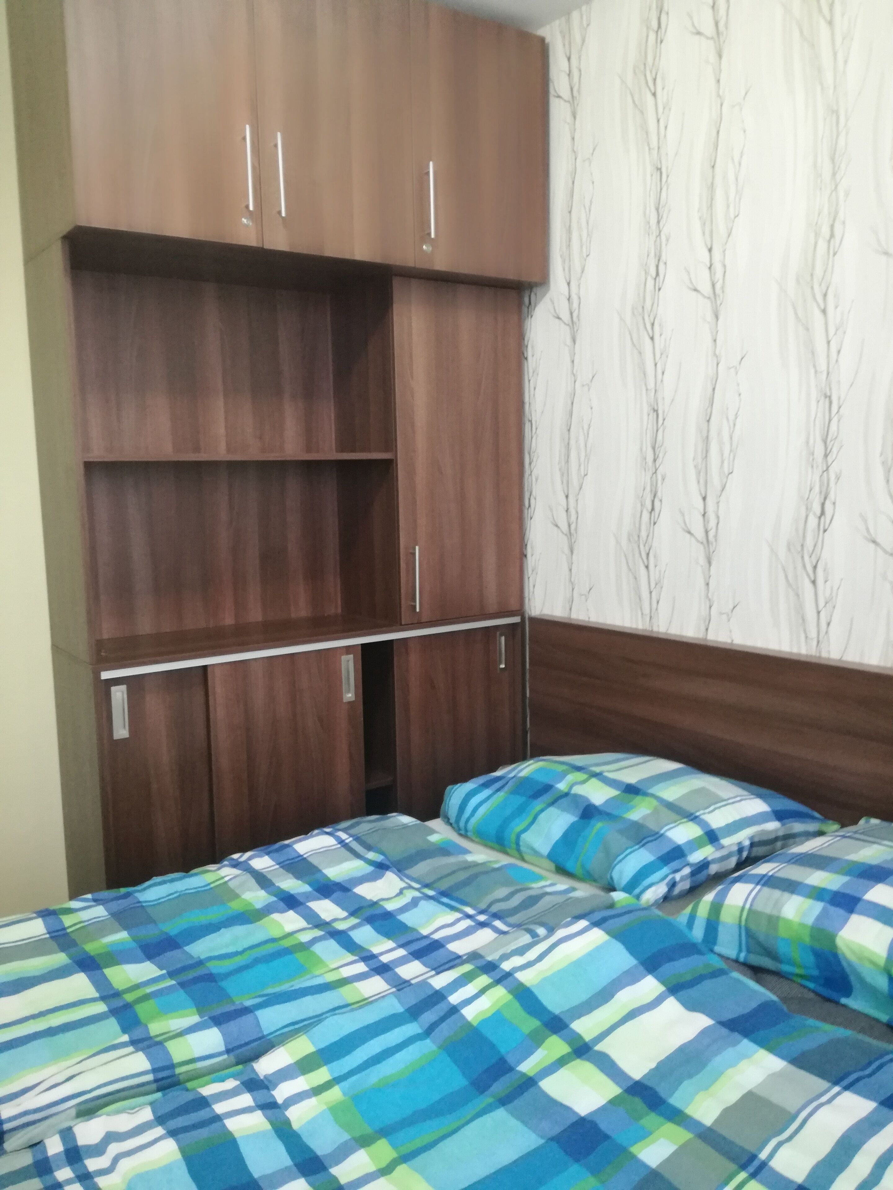 A bedroom with a bed, two pillows, and a wooden wardrobe with multiple compartments.