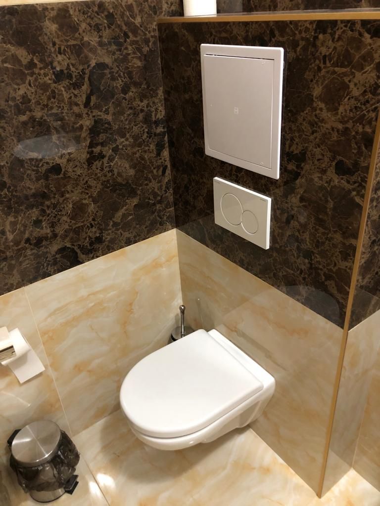 A modern bathroom with a marble floor, a white toilet, and a glass-enclosed shower area.