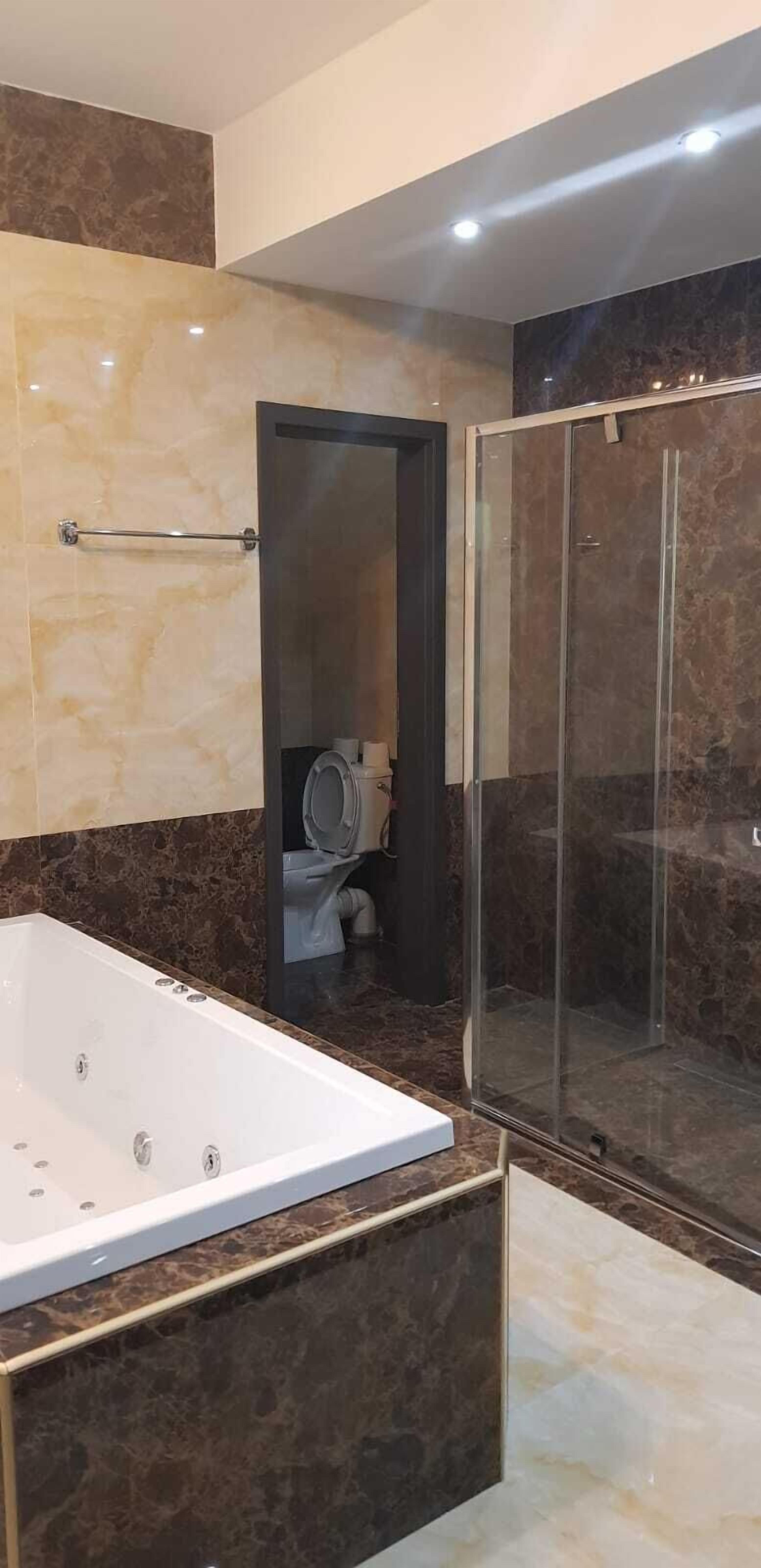 A modern bathroom with a large bathtub, a glass-enclosed shower, and marble walls.