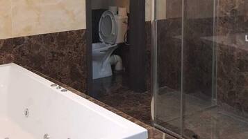 A modern bathroom with a large bathtub, a glass-enclosed shower, and marble walls.