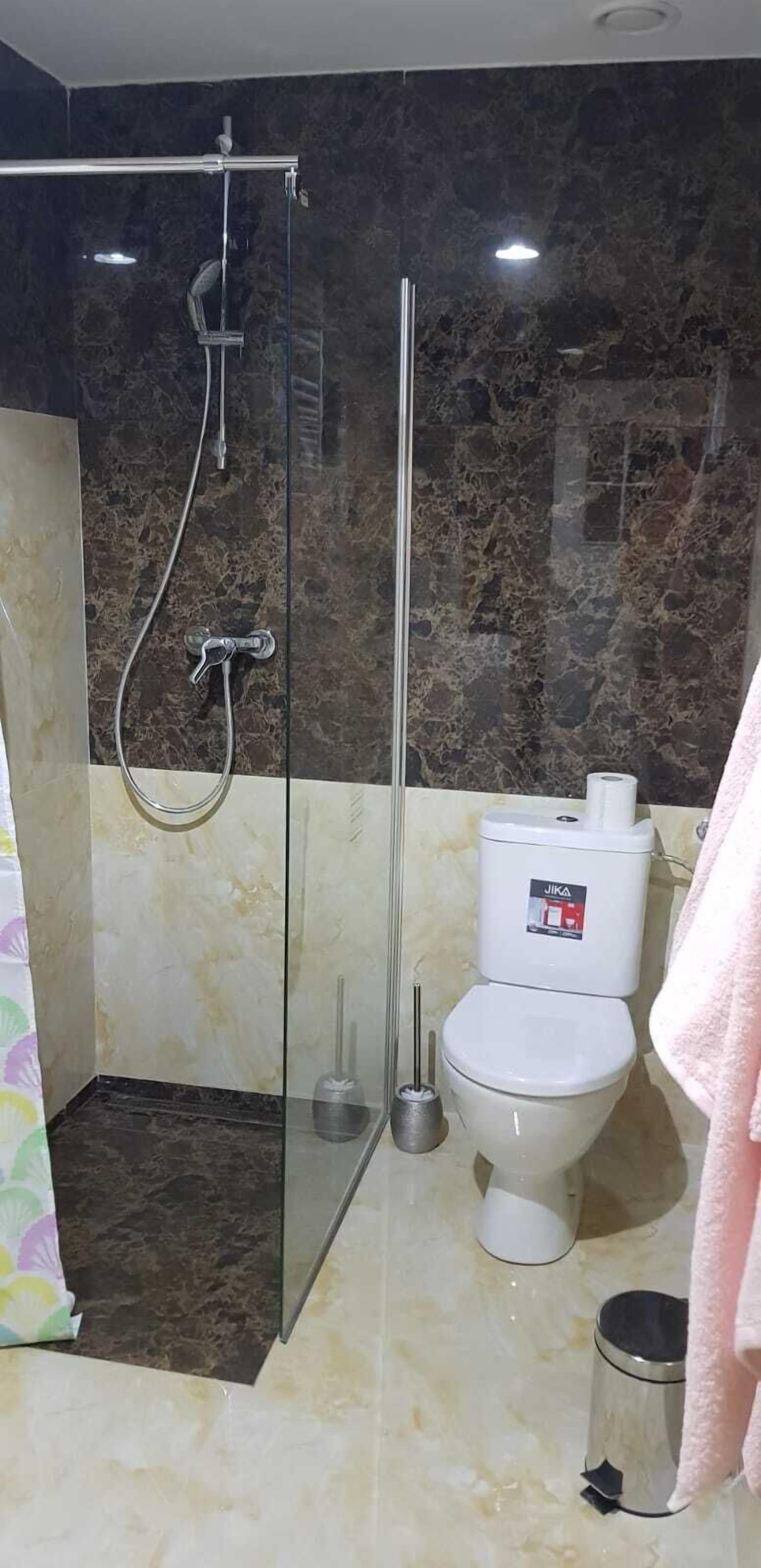 A bathroom with a glass-enclosed shower, a toilet, and a trash can.