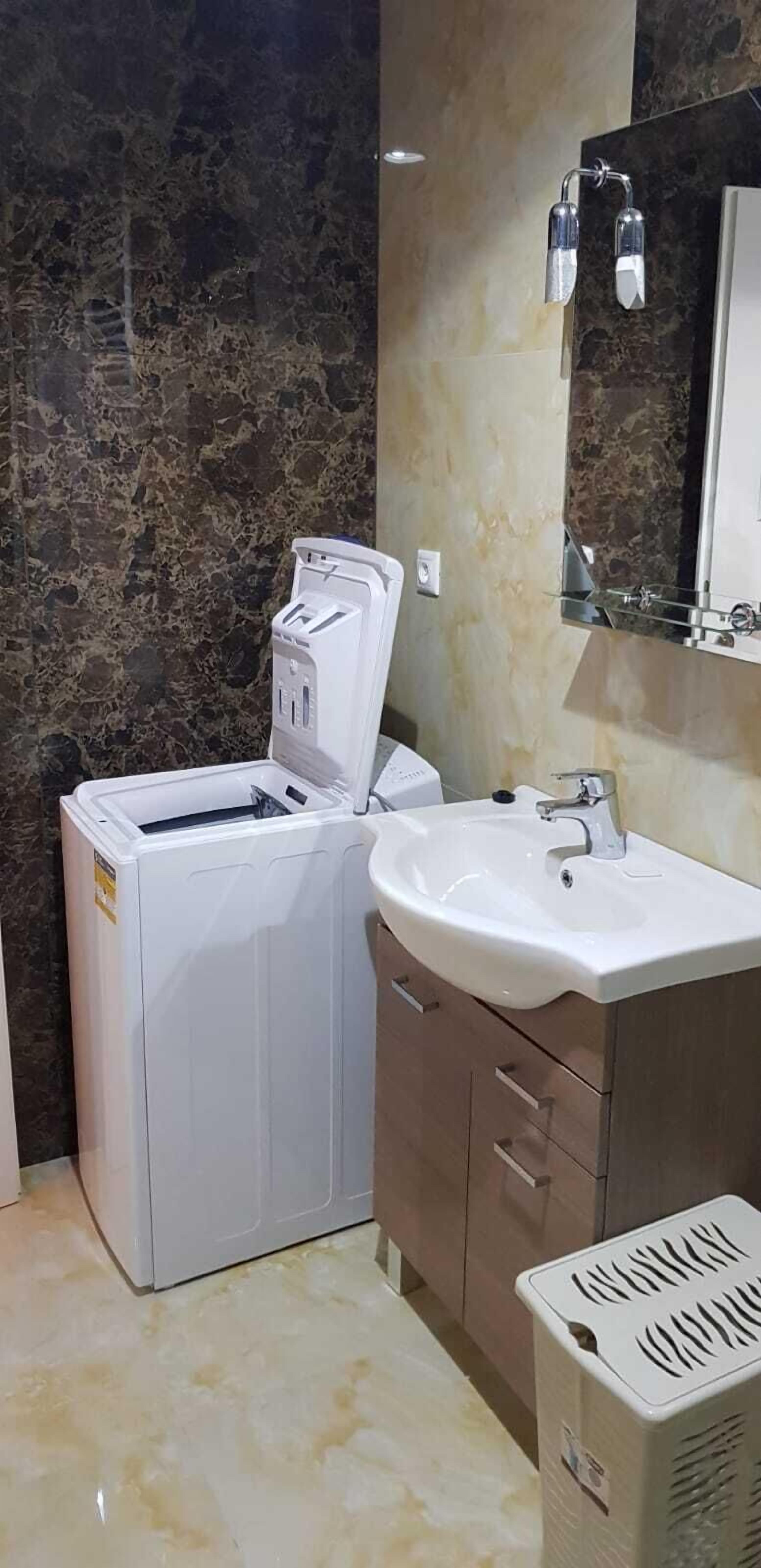 A compact bathroom with a white washing machine, a sink, and a mirror.
