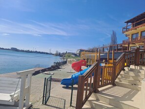 A waterfront park with a playground, including slides and stairs leading to a building with a balcony. - Apartmanovy wellness garni hotel relax (Senec)