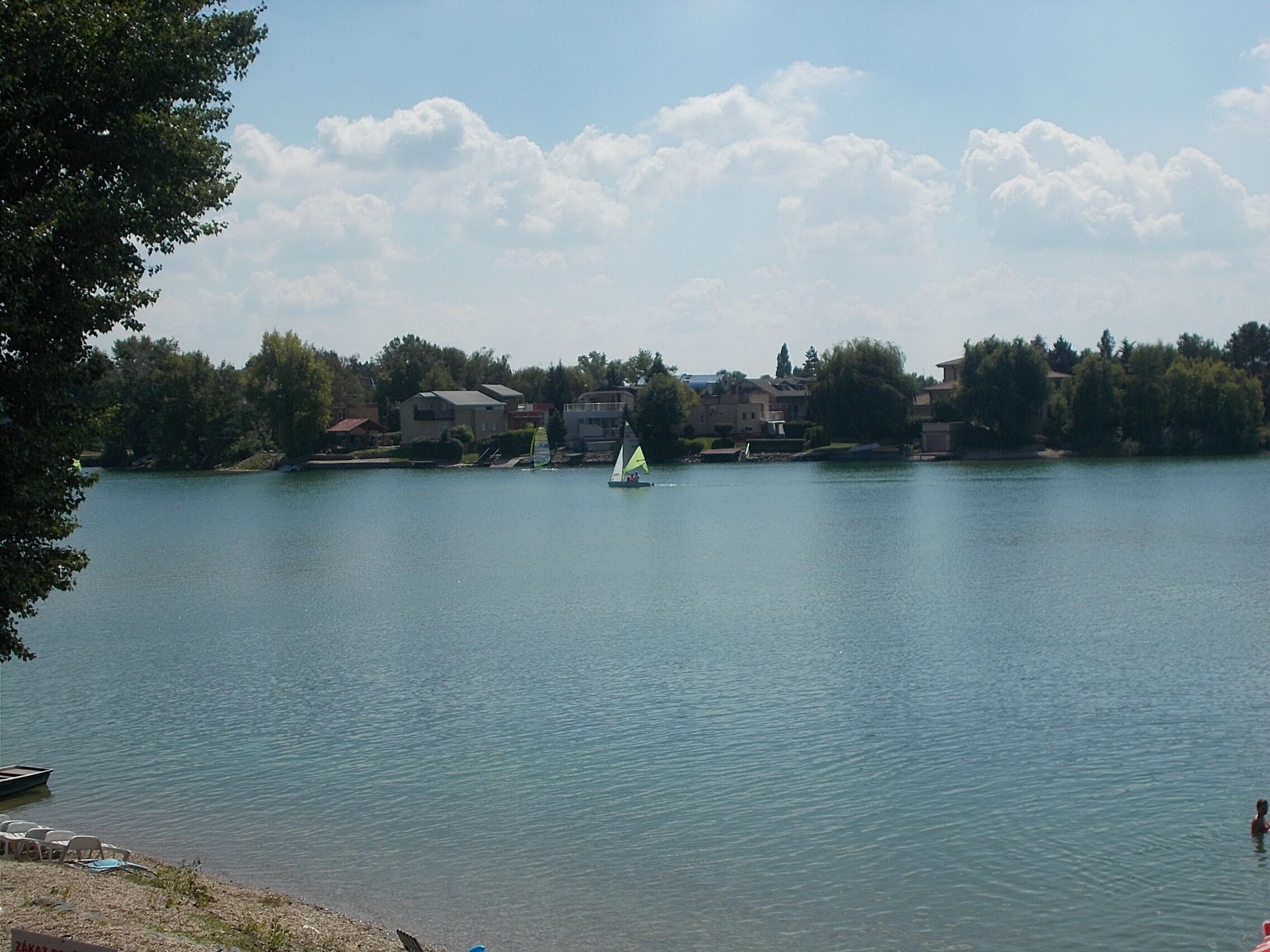 A calm lake with a sailboat, surrounded by houses and trees.