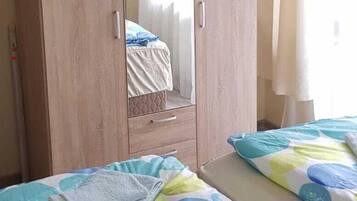 A bedroom with a wooden wardrobe, a bed with a colorful bedspread, and a window with curtains.