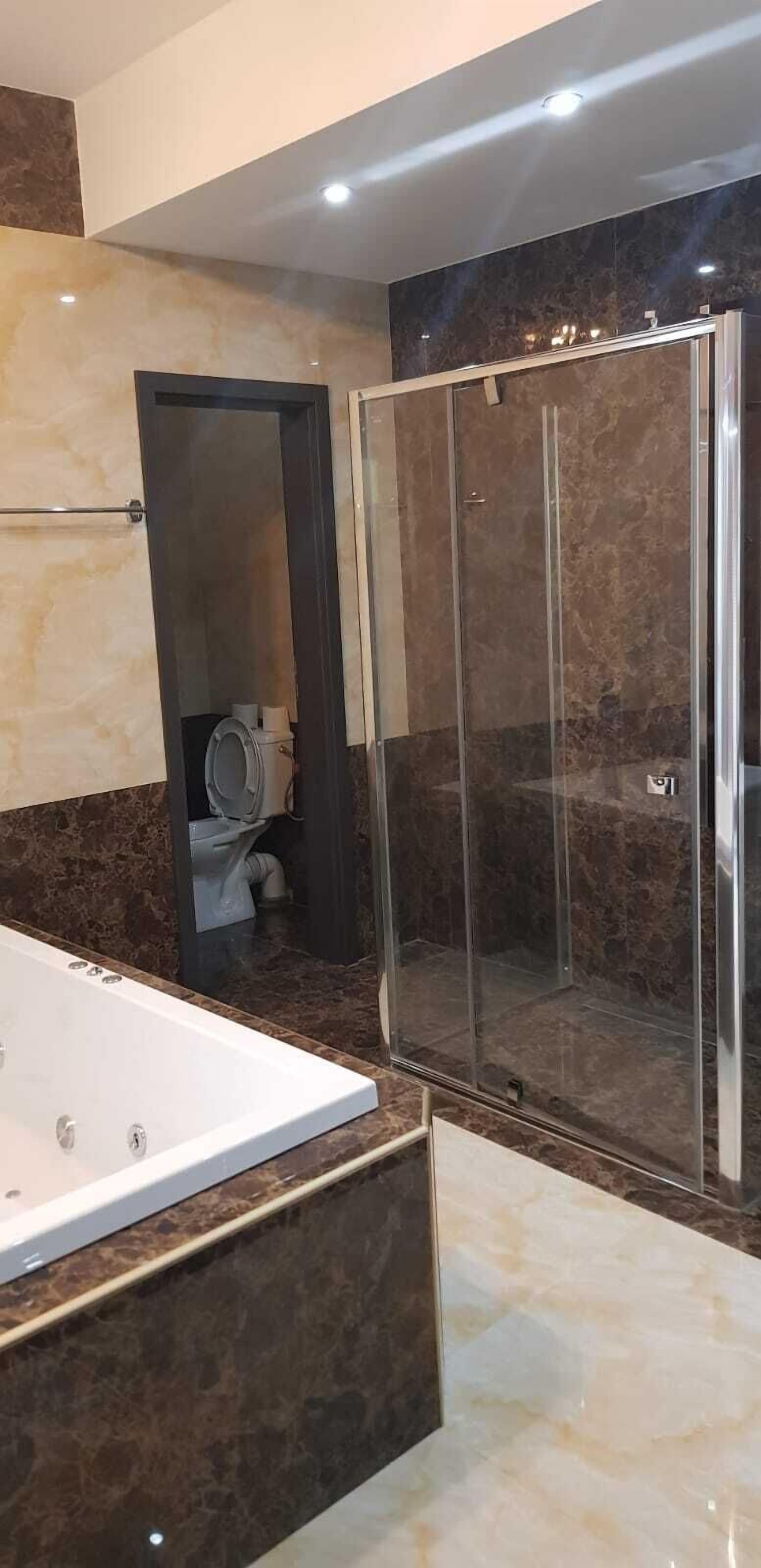 A modern bathroom with a glass-enclosed shower, a bathtub, and marble walls.