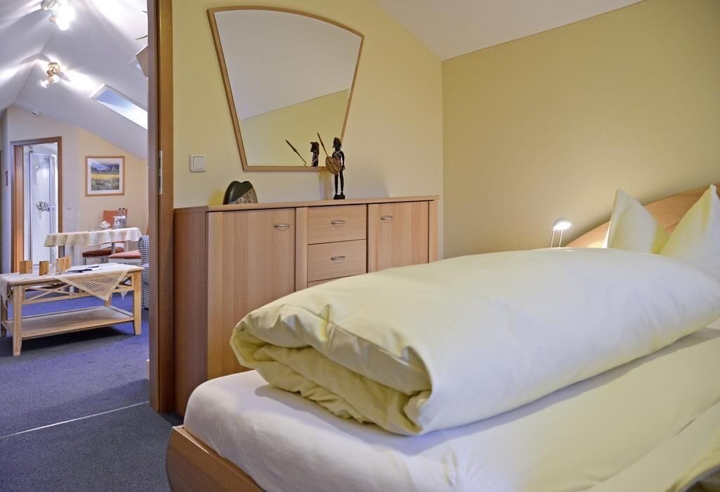 A bedroom with a bed, a wooden dresser, a mirror, and a table with chairs.