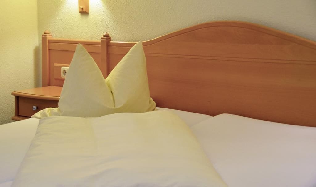 A neatly made bed with two pillows, a wooden headboard, and a nightstand with a lamp.