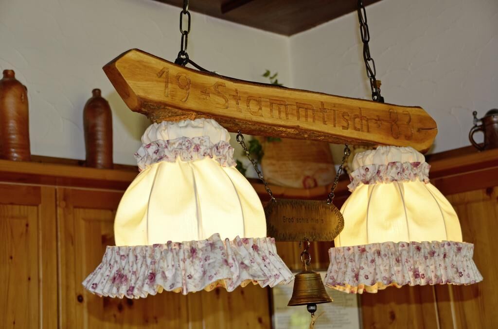 A wooden sign with the inscription "19 St. Antonstr. 83" hanging above two lit lamps with floral-patterned covers.
