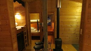 Interior acogedor de una cabaña con detalles de madera, una cama litera, una chimenea y un pequeño rincón de descanso.