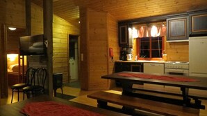 Interior de una cabaña de madera con comedor, cocina y chimenea.