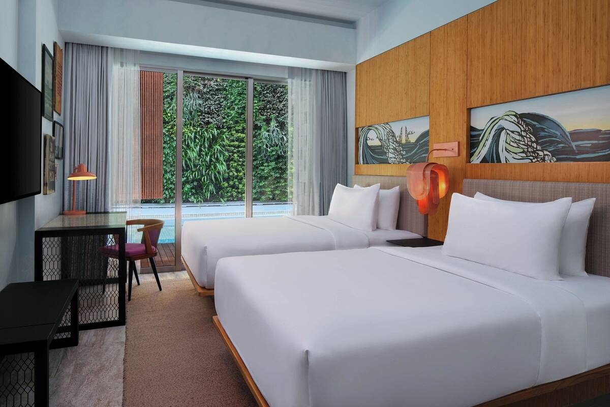 A hotel room with two beds, a desk, a chair, a TV, and large windows with curtains.