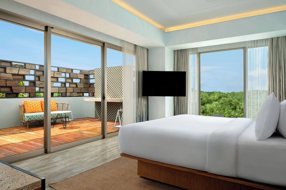 A modern hotel room with a large bed, a TV, and a balcony with a seating area.