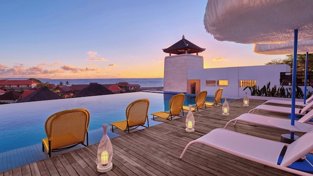 A poolside area with lounge chairs and lanterns, overlooking a body of water and a distant shoreline. - Aloft by Marriott Bali Seminyak (Keroboken Kelod)
