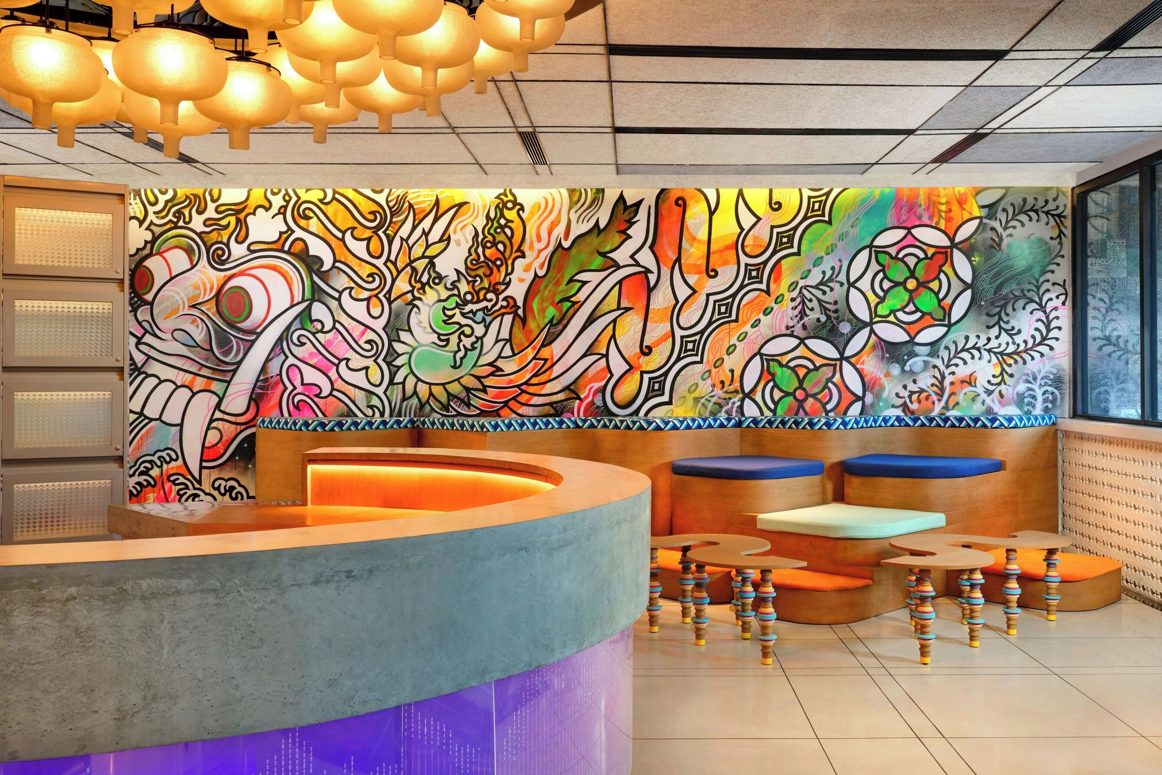 Een modern interieur met een kleurrijke muurschildering, een receptiebalie en zithoeken.