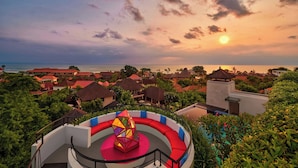 A resort with a circular outdoor seating area, a pool, and a view of the ocean at sunset. - Aloft by Marriott Bali Seminyak (Keroboken Kelod)