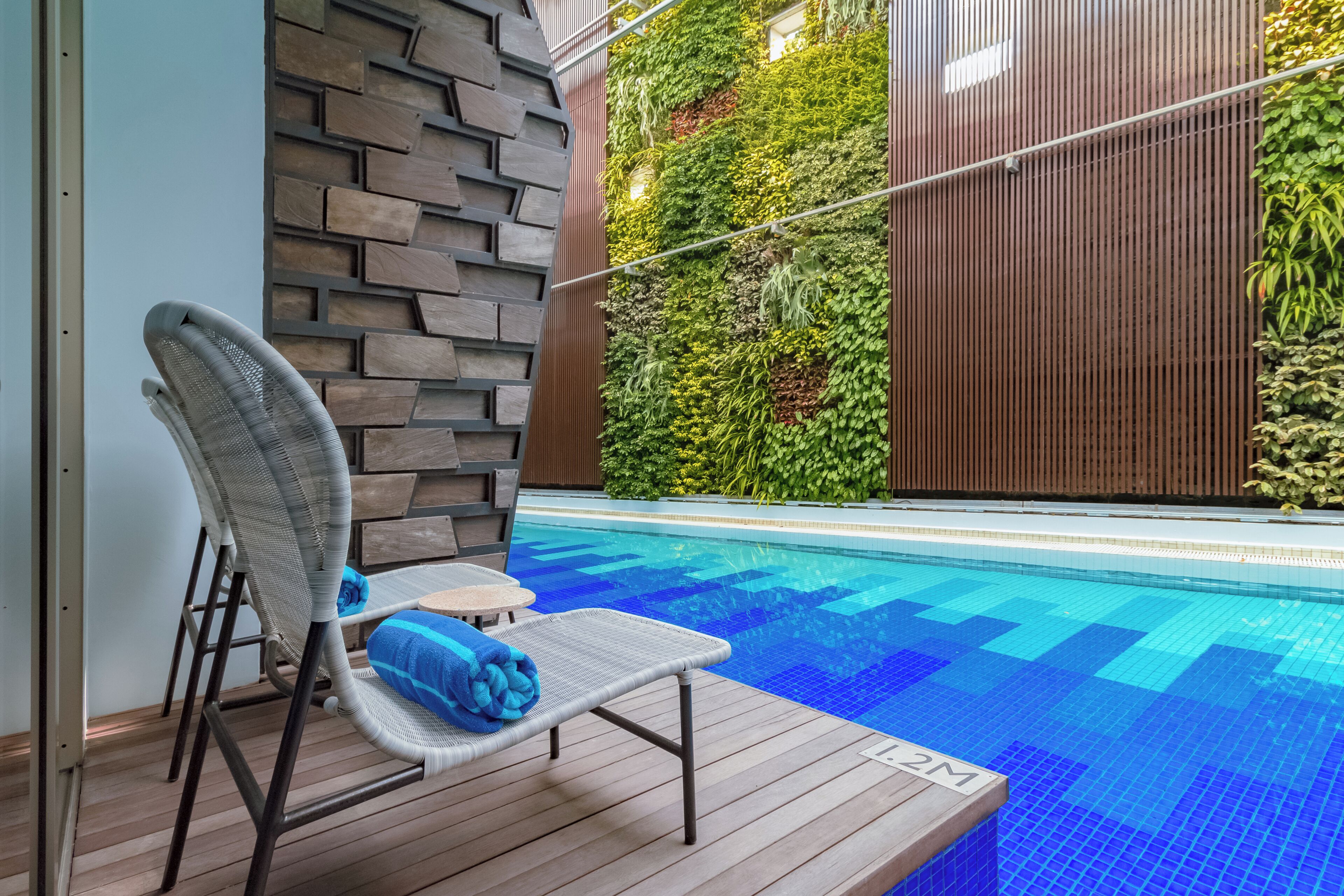 Un área junto a la piscina con una silla de descanso, una mesita y una terraza de madera.