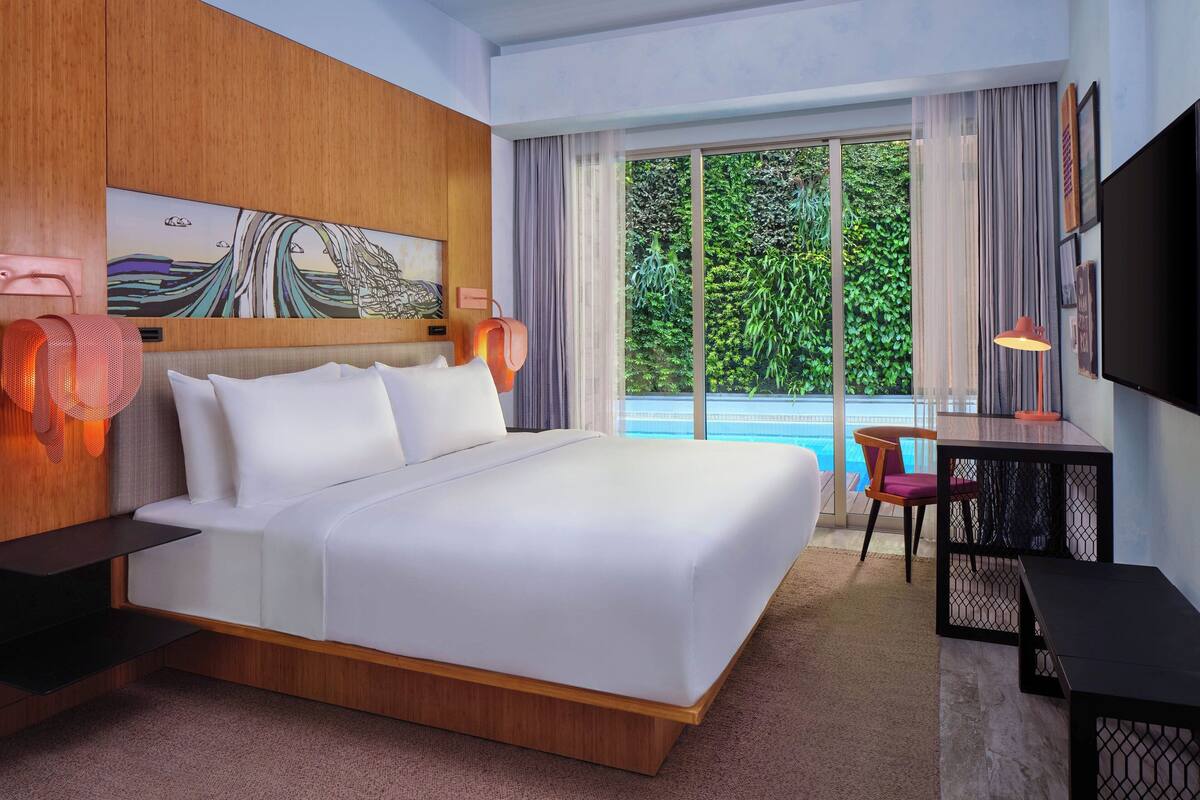 A modern hotel room with a large bed, a desk, and a view of the outdoors.